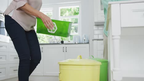 senior diverse couple wearing shirts and segregating waste in kitchen