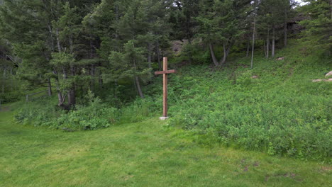cruz cristiana de madera en el borde de un bosque y campo de hierba verde abierto