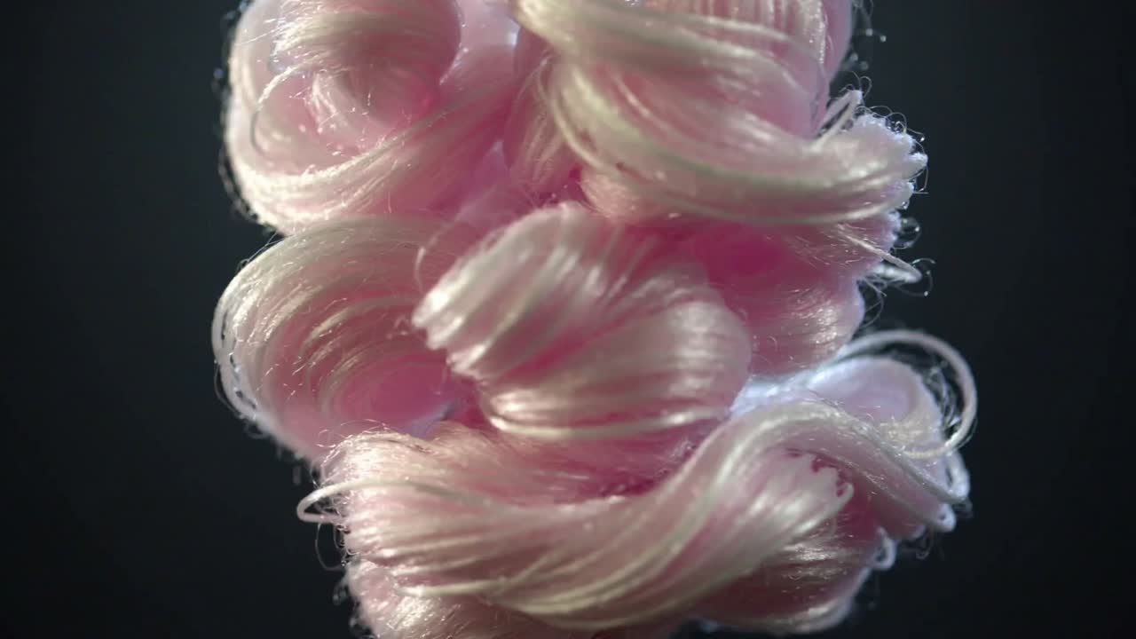 Spinning glossy pink fiber cluster opening in studio on release, showing center hole and fibers