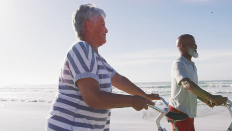 smiling senior african american couple walking with bicycles at the beach
