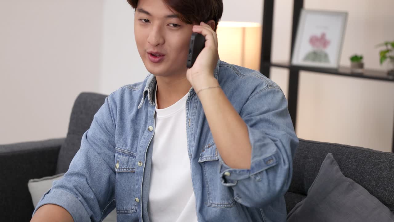 ชายหนุ่มชาวเอเชียคนหนึ่งนั่งอยู่บนโซฟา คุยโทรศัพท์สมาร์ทโฟนด้วยสีหน้าตั้งใจ