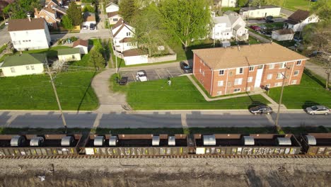 Train-with-steel-coils-passing-through-peaceful-town-of-Wyandotte,-aerial-side-fly
