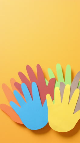 vertical video of hands together made of colourful paper on yellow background with copy space