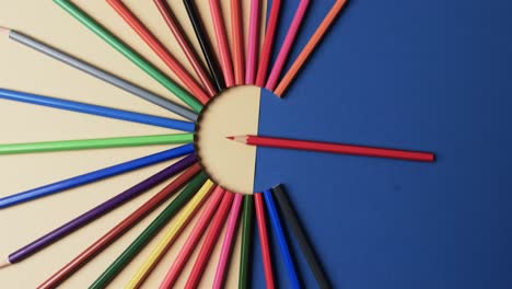 Overhead-view-of-crayons-arranged-on-beige-and-blue-background,-in-slow-motion