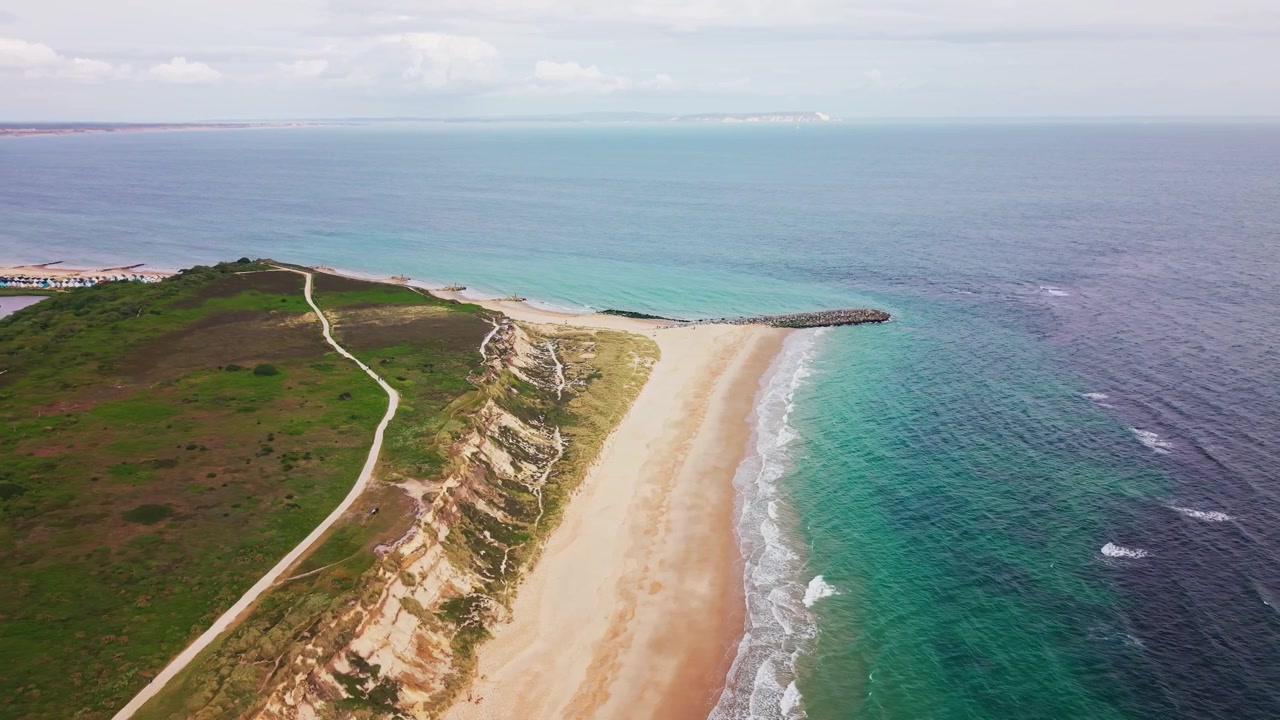 Droneoptagelse langs Hengistbury Head med sandstrand, turkisblåt hav, kystklipper, hedestier, stenkaj og fjerne Isle of Wight kystlinje