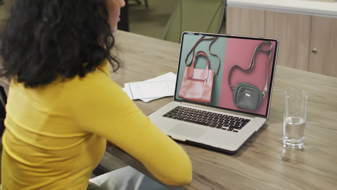 mujer biracial en la mesa usando portátil, compras en línea de bolsos, cámara lenta