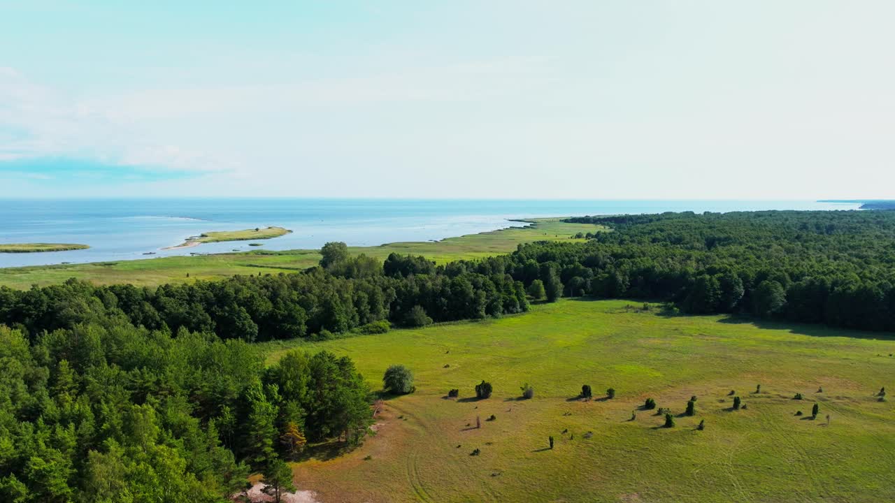 Flying over coastal countryside with trees and fields, islands visible in the sea.