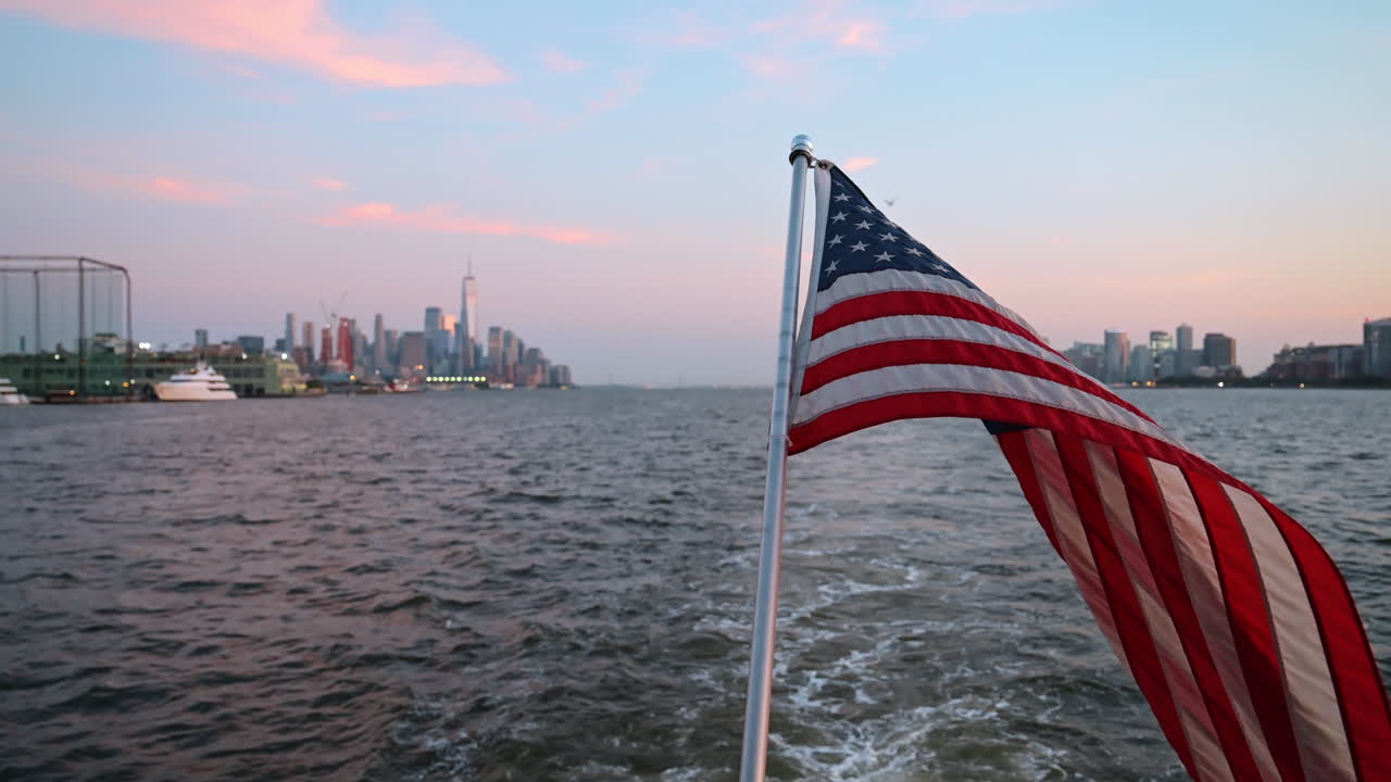 Vista del tramonto sullo skyline di New York da una barca con bandiera americana sull'acqua. Una barca naviga sull'acqua con una bandiera americana che sventola. Lo skyline di New York si staglia sullo sfondo al tramonto