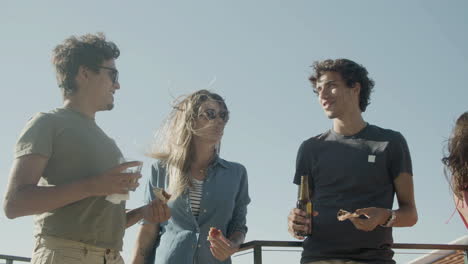 carefree friends talking together while eating pizza and drinking beer during a rooftop party