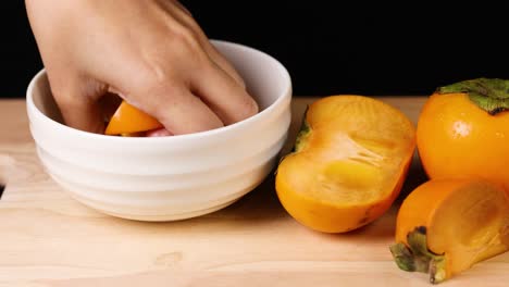 hand selects persimmon from a white bowl