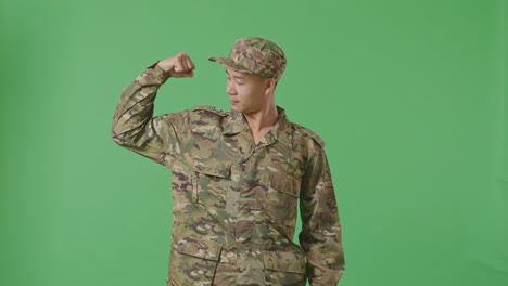 asian man soldier smiling and flexing his bicep while standing in the green screen background studio