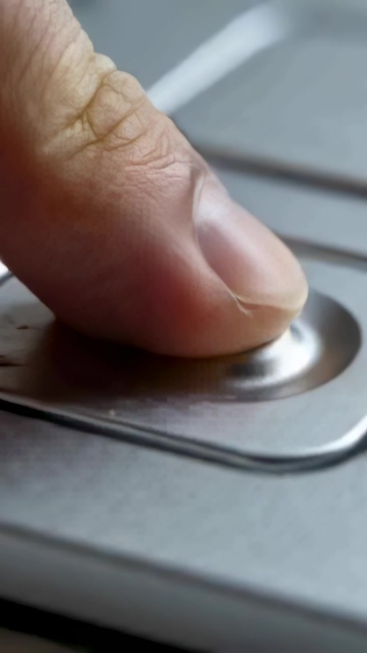 Vertical video: Approaching fingertip pressing recessed button on metal plate, starting device