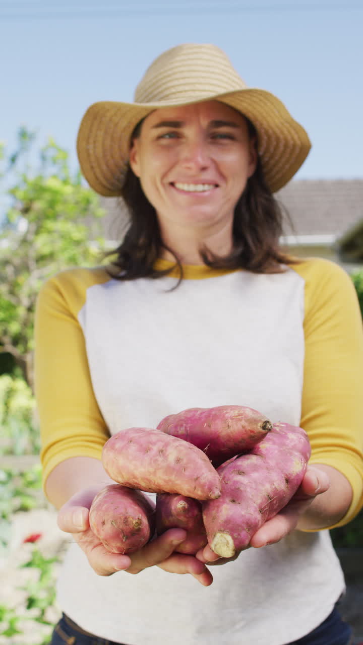 video vertical de una mujer caucásica sonriente en un jardín soleado llevando remolachas recién cosechadas