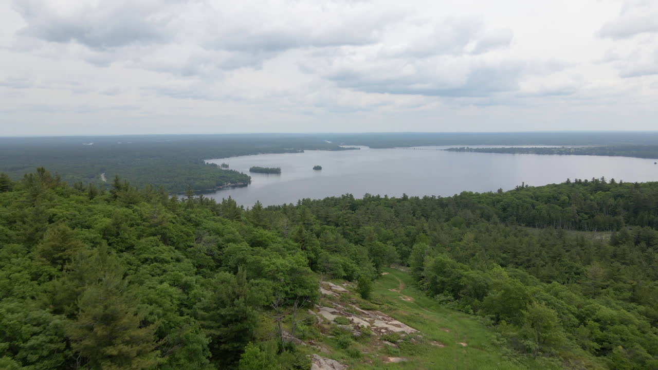 Aerial shot over thick green forest covered mountain into a calm lake and islands on an overcast day. Calabogie Ontario