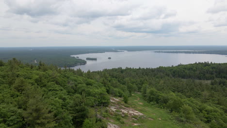 aerial shot over thick green forest covered mountain into a calm lake and islands on an overcast day. calabogie ontario