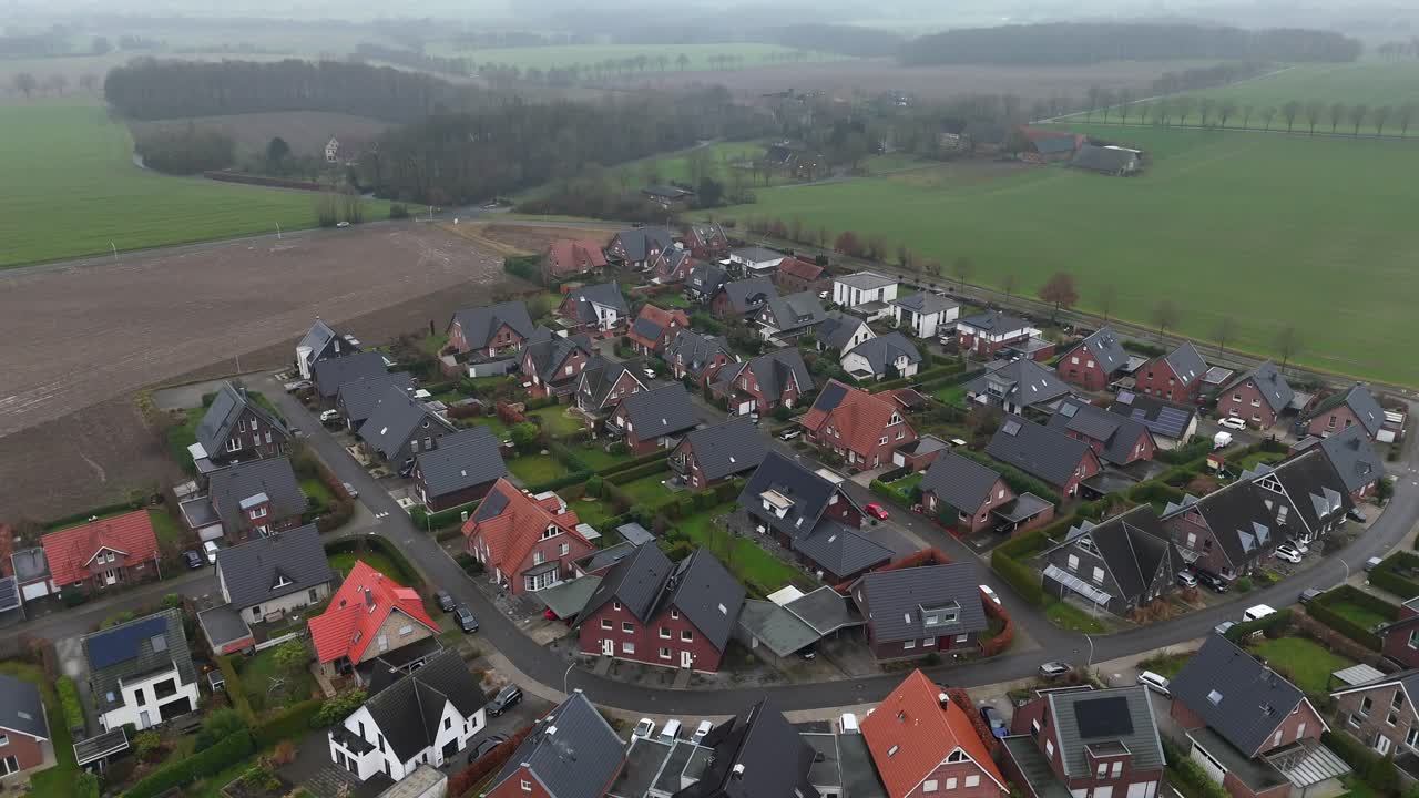 Small Village with single family houses in american countryside during foggy day. Winter season in suburb district of City. Aerial top down flyover. Forest landscape and cars on road in distance.