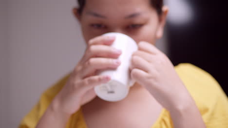 holding a ceramic mug as the woman is sipping some hot beverage while closing her eyes as she savors what she is drinking