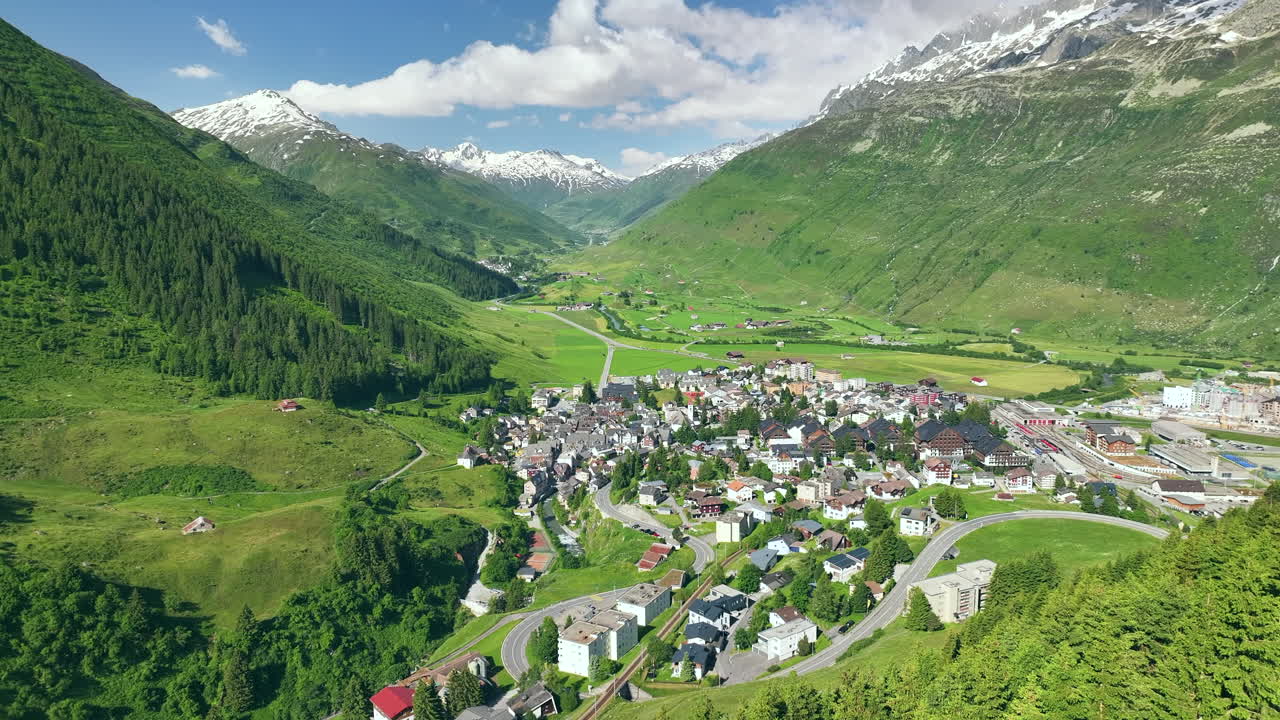 Stunning aerial view of Andermatt, a village in Switzerland, located at base of vibrant green mountains and snow capped peaks