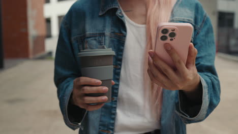 woman using smartphone and holding a reusable coffee cup outdoors