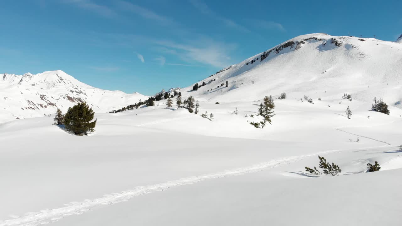 Low drone flyover of snowy mountain ranges with a couple of hiking paths in Warth, a small municipality in Vorarlberg, Austria on a sunny day with clear blue skies in 4K