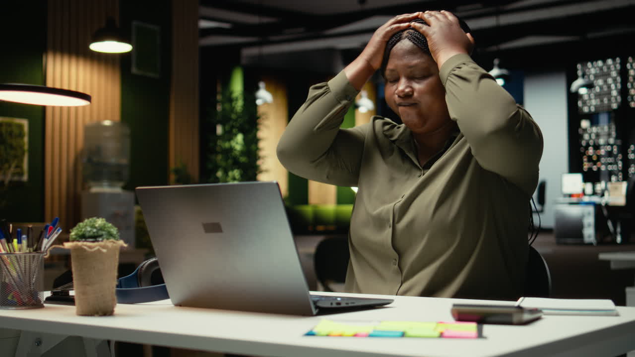 Black female assistant tensed and burdened in dark office after hours
