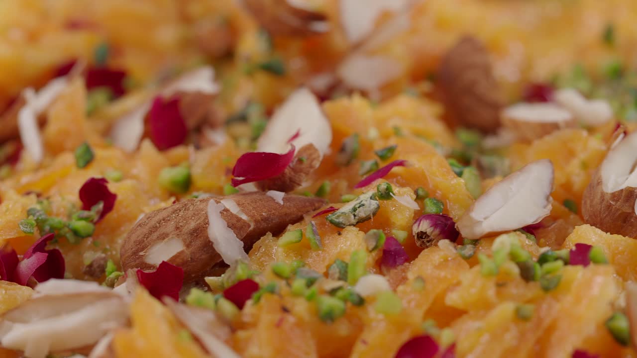 Primo piano di Halwa arancione tradizionale guarnito con frutta secca e petali di rosa