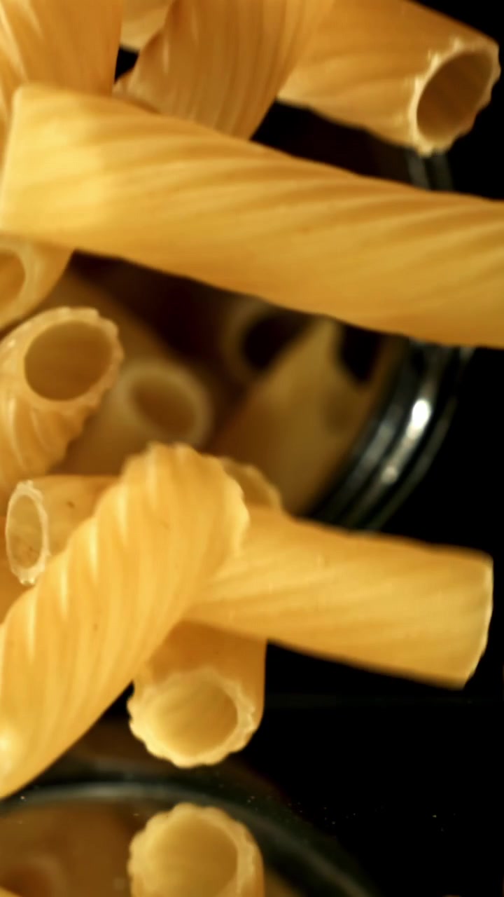 Rigatoni secchi che cadono al rallentatore su uno sfondo scuro