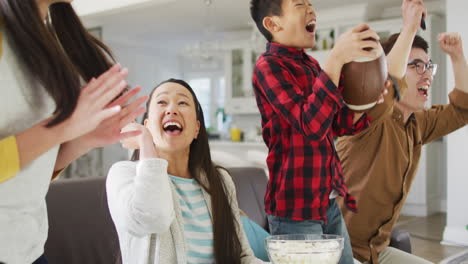 excited asian parents with daughter and son with american football watching sport on tv and cheering