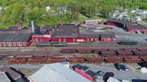 an aerial view of an abandoned narrow gauge coal rail road with rusting hoppers and freight cars and support building starting to be restored