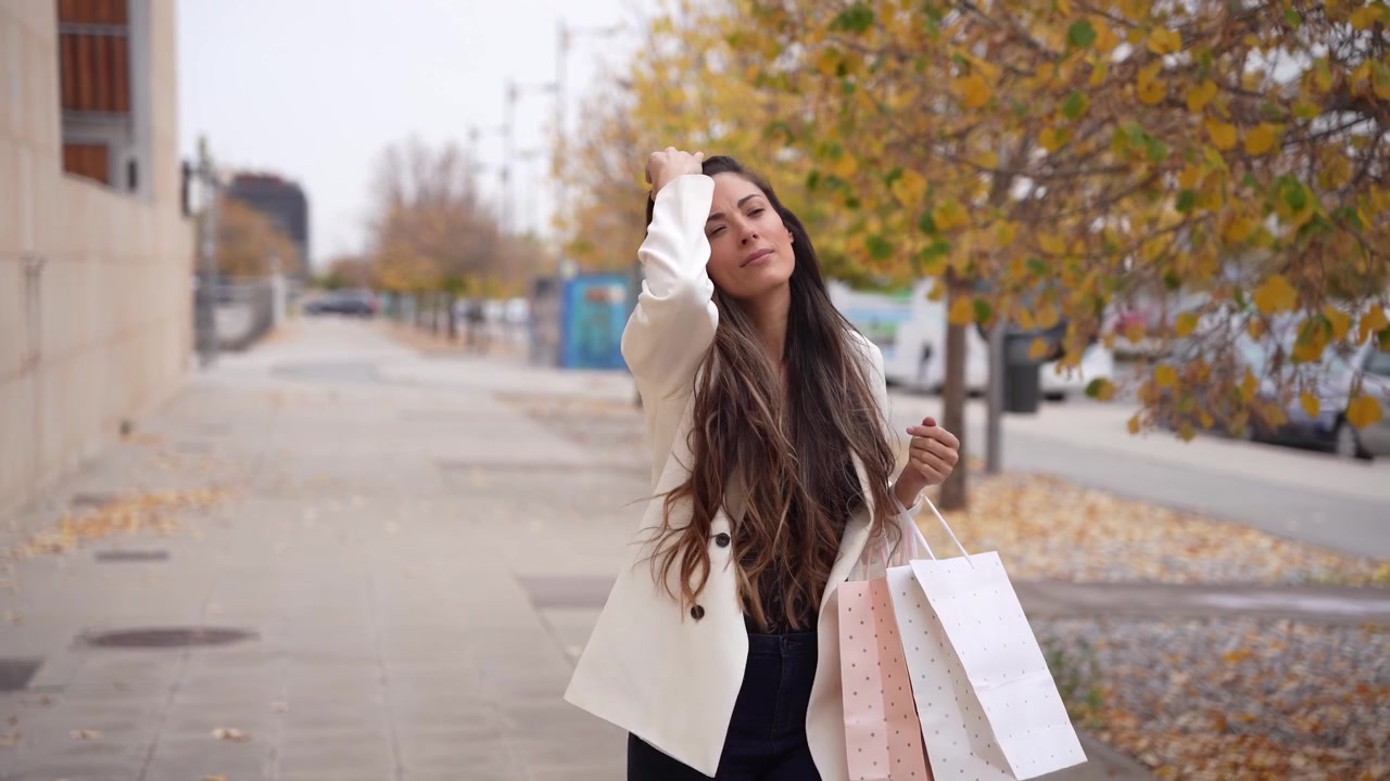 Una donna elegante si gode lo shopping in una vivace strada cittadina mentre usa uno smartphone.