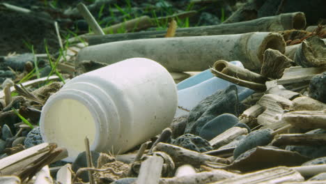 Deep-focus-shot-of-a-washed-up-plastic-battle-lying-on-a-beach-surrounded-by-other-plastic-and-driftwood