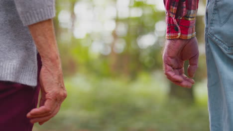 close up of loving retired senior couple holding hands hiking in woodland countryside together