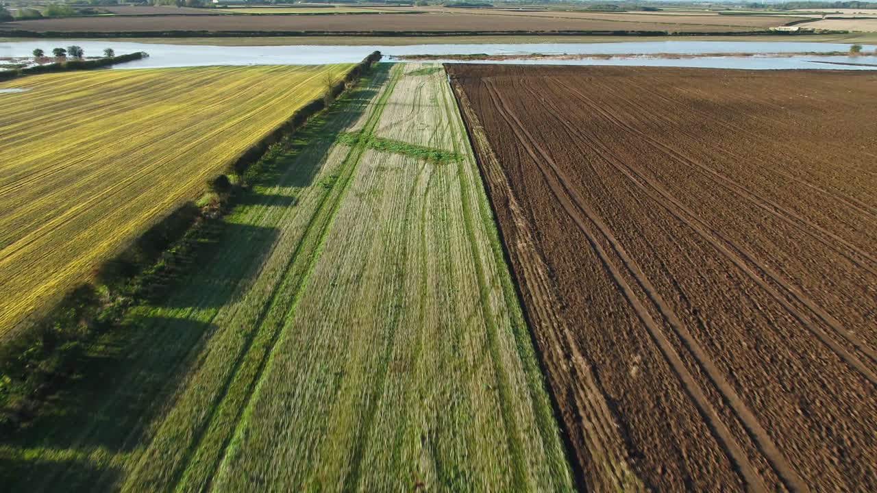 Aerial drone footage flying over multi-coloured farmer's harvested fields, hedgerows and a flooded field in North Yorkshire, UK on a beautiful, sunny autumn morning