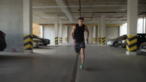 Athlete-runs-inside-the-empty-parking-garage,-front-view