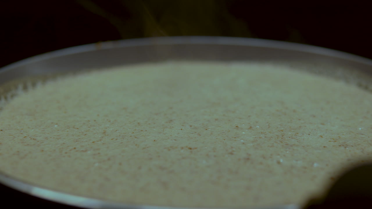Macro della pastella liquida per pancake che cuoce su una piastra calda. Perfetto per tutorial culinari, sequenze di preparazione della colazione e contenuti per l'industria alimentare