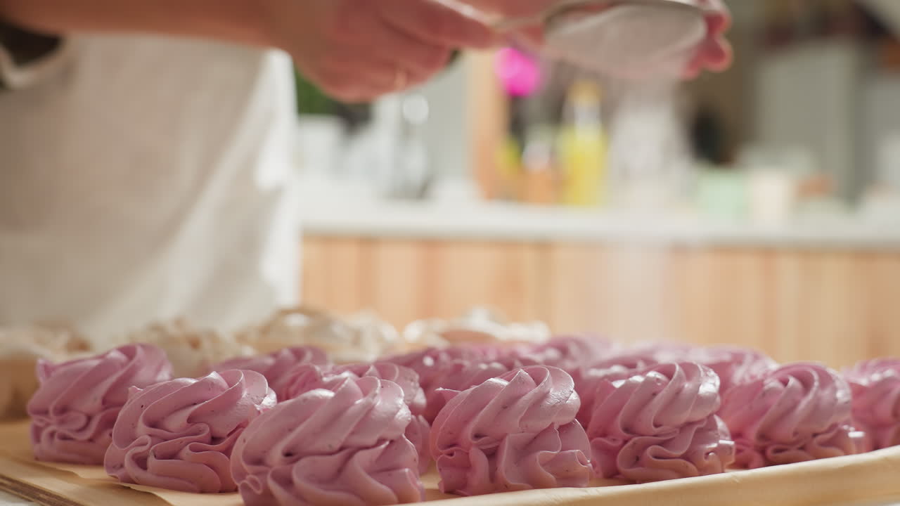 Close up of beautifully arranged swirl pink cupcakes on parchment paper as caterer sprinkles flour over them in warm kitchen setting, capturing delicate texture, detail, and baking atmosphere