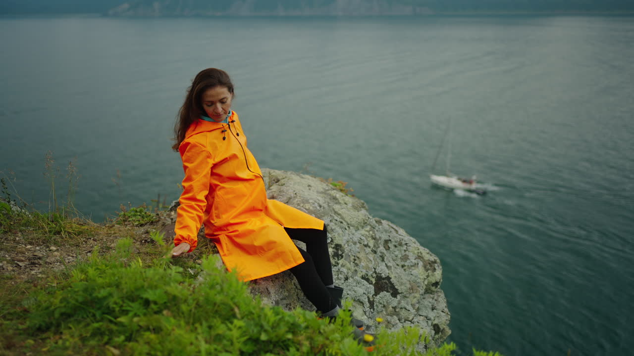 Woman in an Orange Rain Jacket on a Cliff overlooking a Lake