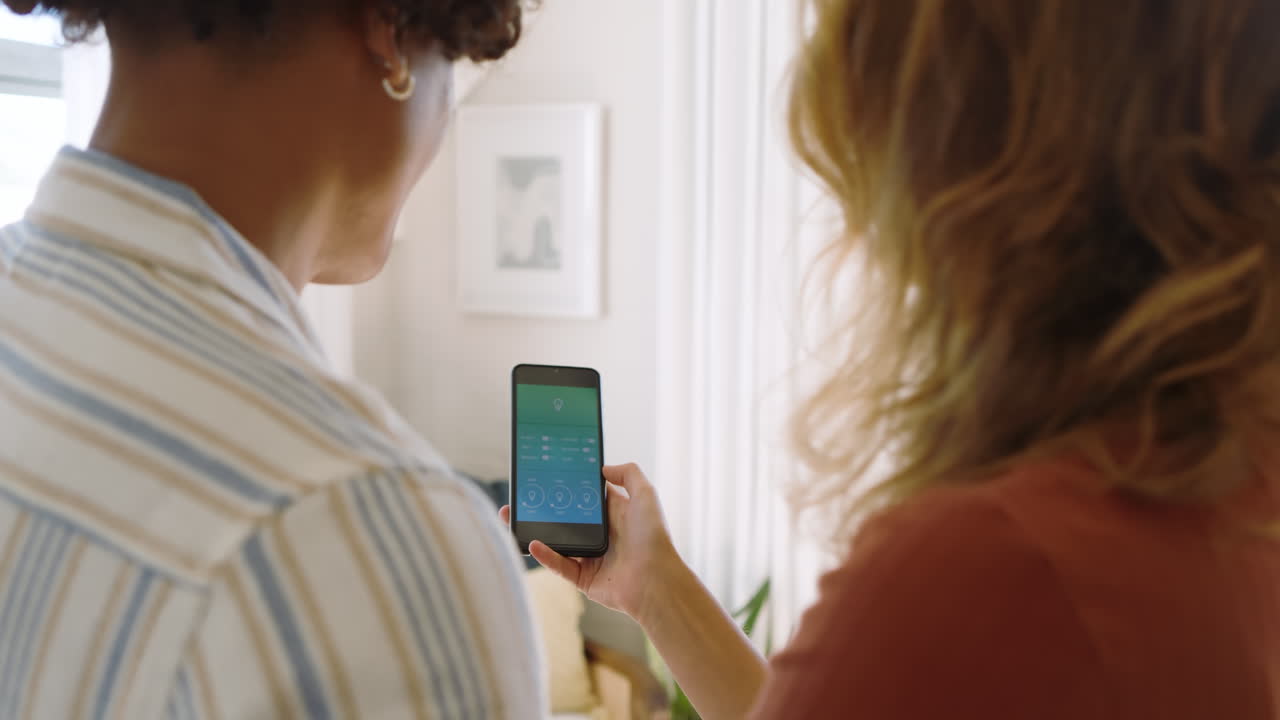 Diverse couple using smartphone to control smart home devices in living room