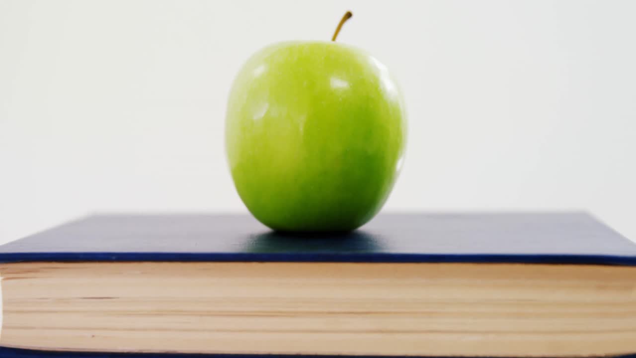 manzana verde en una pila de libros contra un fondo blanco