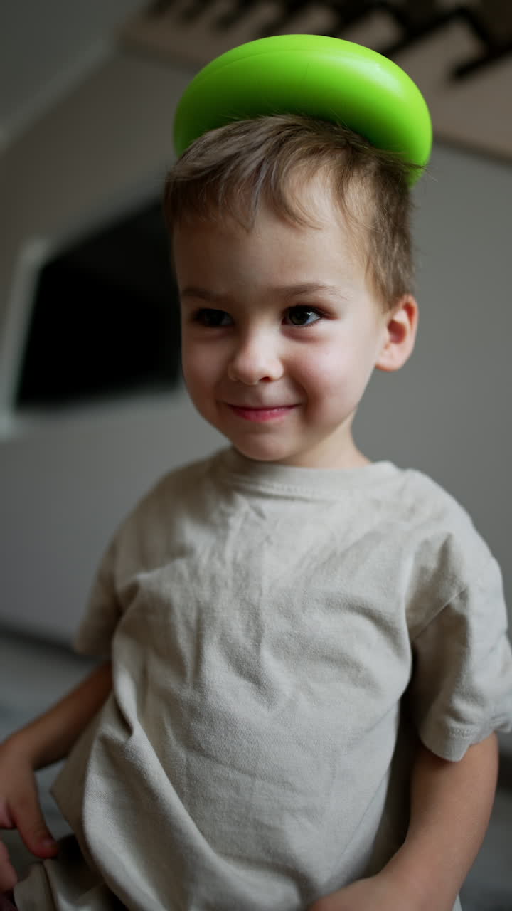 Funny toddler boy plays cheerfully at home. Kid puts a green pyramid detail on his head and drops it. Vertical video.