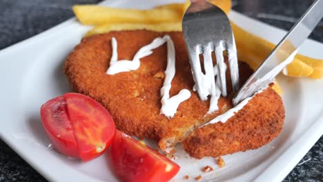 cerca de una chuleta de pollo crujiente con papas fritas, tomate y salsa blanca