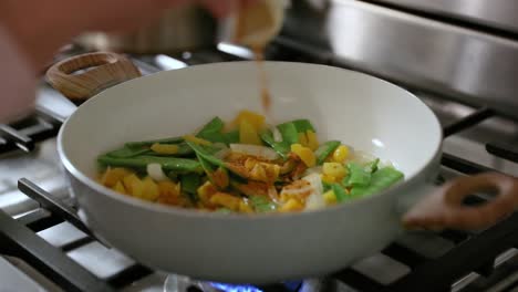 woman adding spice to frying pan of cooking vegetables in slow motion