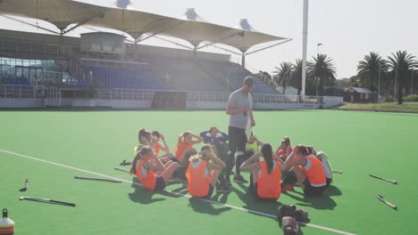 Coach-watching-female-hockey-players-exercising-on-the-field