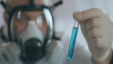 cerca en el laboratorio un hombre en una pantalla de respirador de vidrio sostiene un tubo de vidrio con un líquido azul contra el virus y lo mira. imágenes de alta calidad 4k