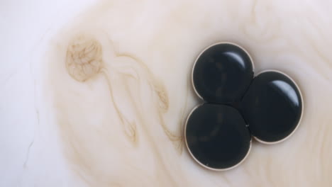 macro shot of three black bubbles bursting into a light brown liquid