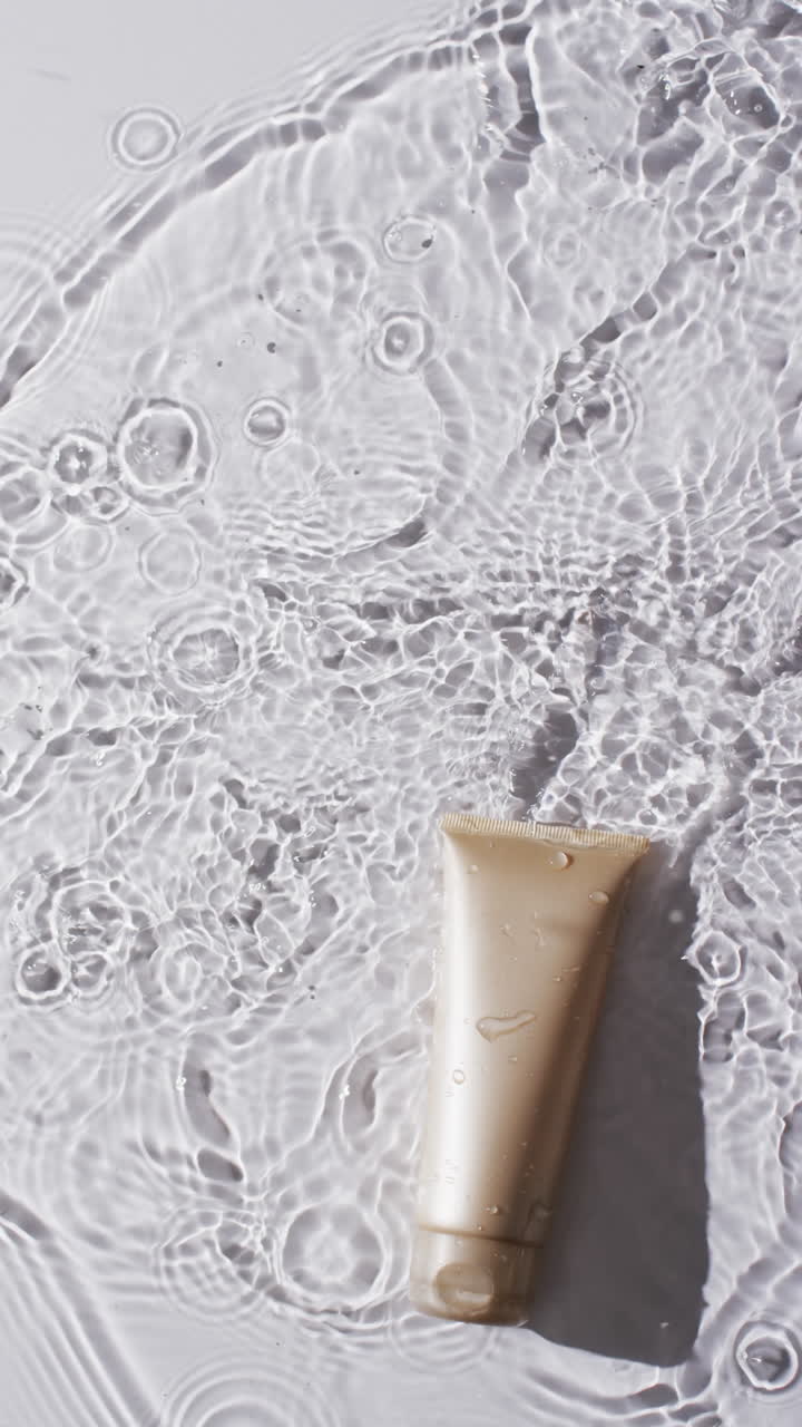 Vertical video of beauty product tube in water with copy space on white background