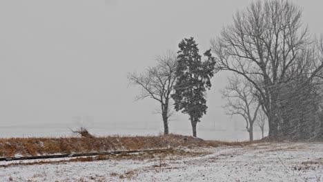 a view of a winter snow storm with blowing winds and snow over farmlands and a rail road track