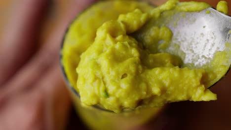 scooping mixing yellow avocado puree with spoon into glass pot, close up