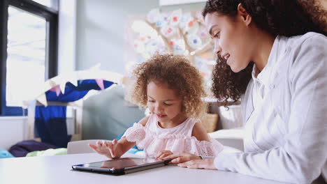 Female-infant-school-teacher-working-one-on-one-with-a-young-mixed-race-schoolgirl-using-tablet,-close-up