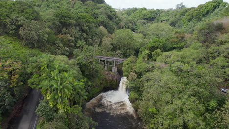 Fly-above-tropical-landscape,-dense-lush-green-vegetation-and-waterfall-on-small-river